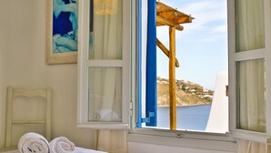 Quarto com cama, janela com vista para a paisagem costeira e um quadro na parede.
