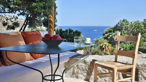 Uma mesa com uma tigela de frutas, um copo d'água e uma xícara, com vista panorâmica para o mar.