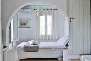 A bedroom with a bed, a window with sheer curtains, a framed picture on the wall, and a white wardrobe. - Villa Athena (Mykonos)