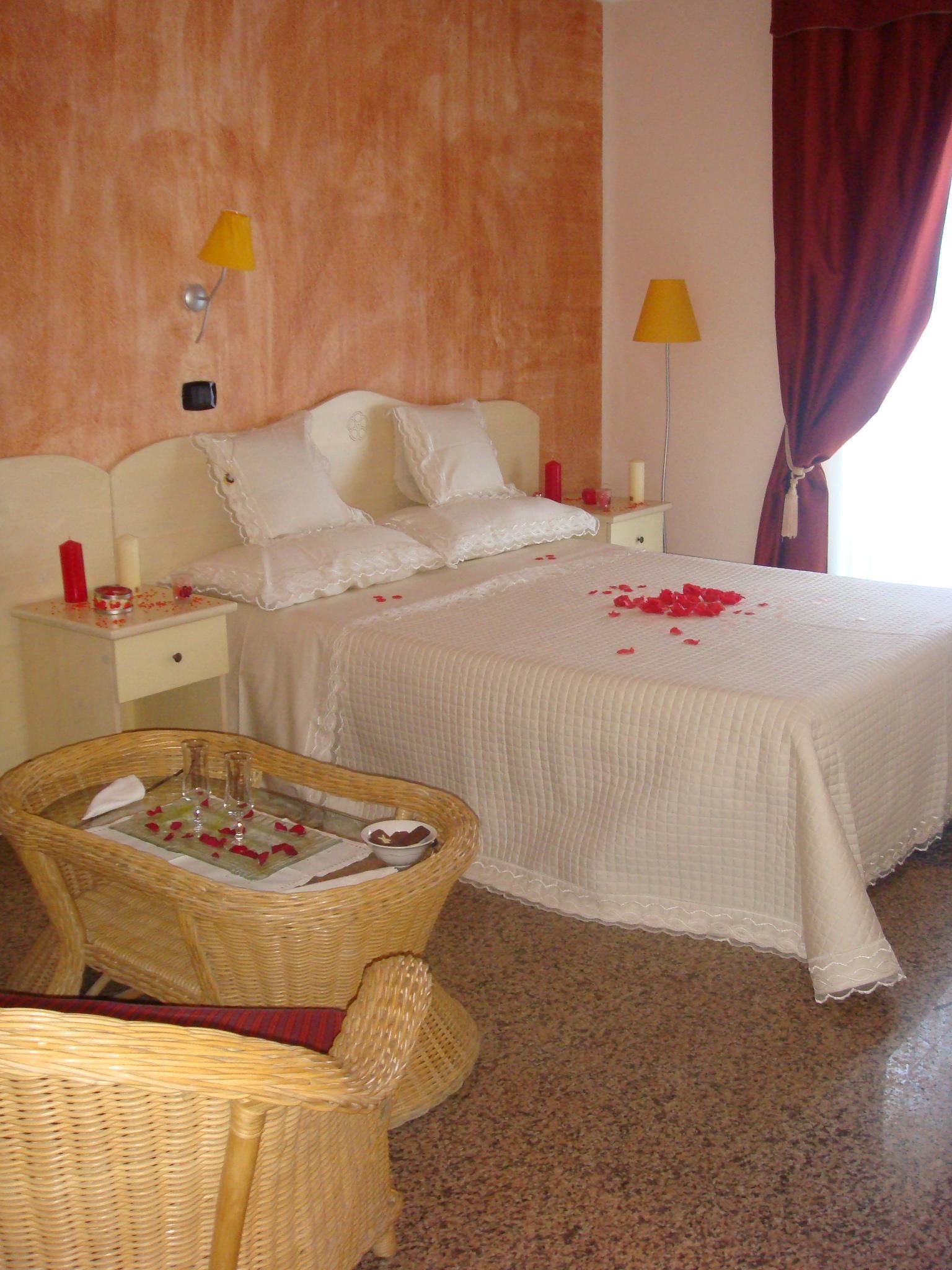 A hotel room with a bed, two bedside tables, a wicker chair, and a large window with curtains.