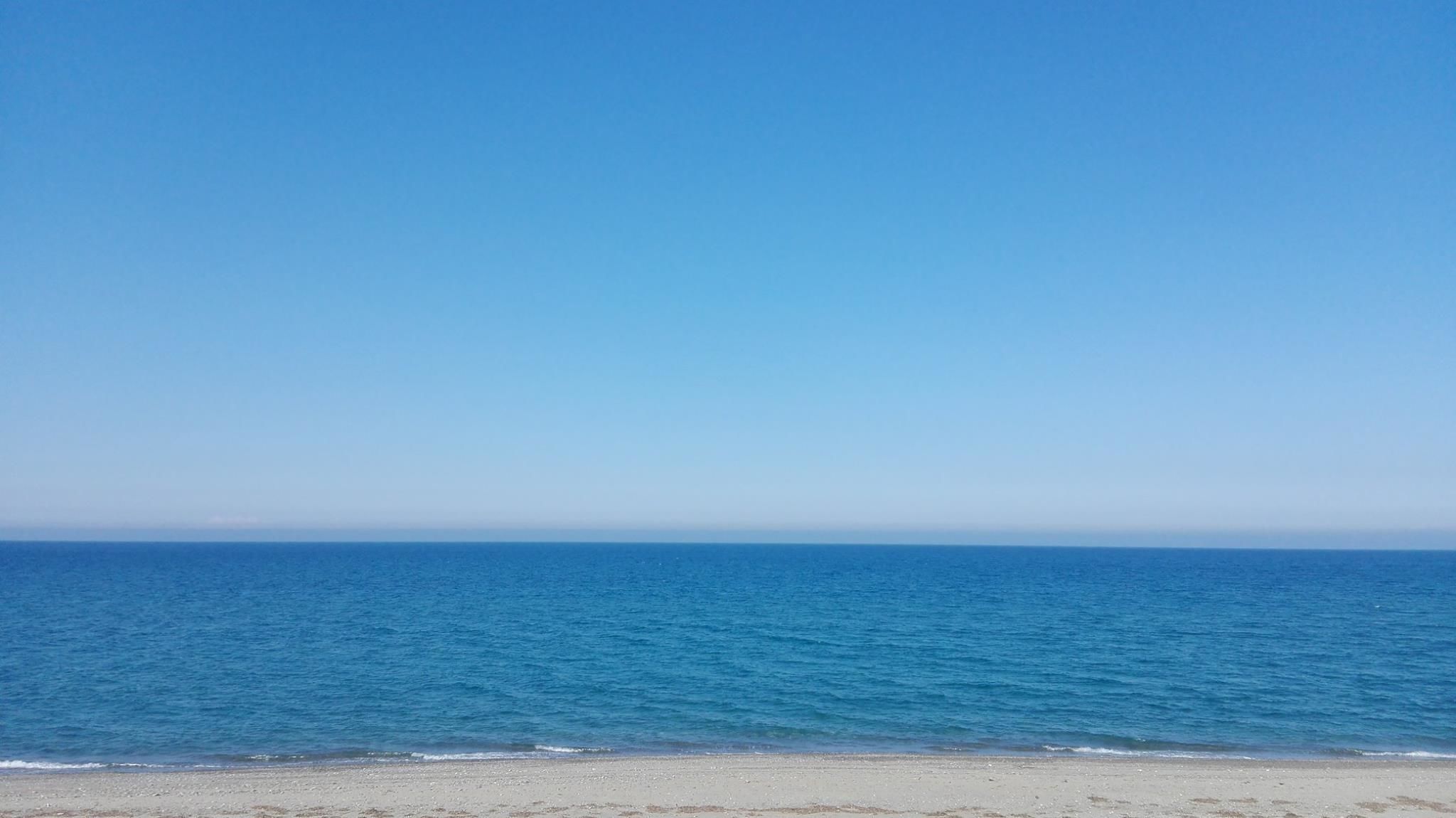 A beach with clear blue water and a sandy shore.