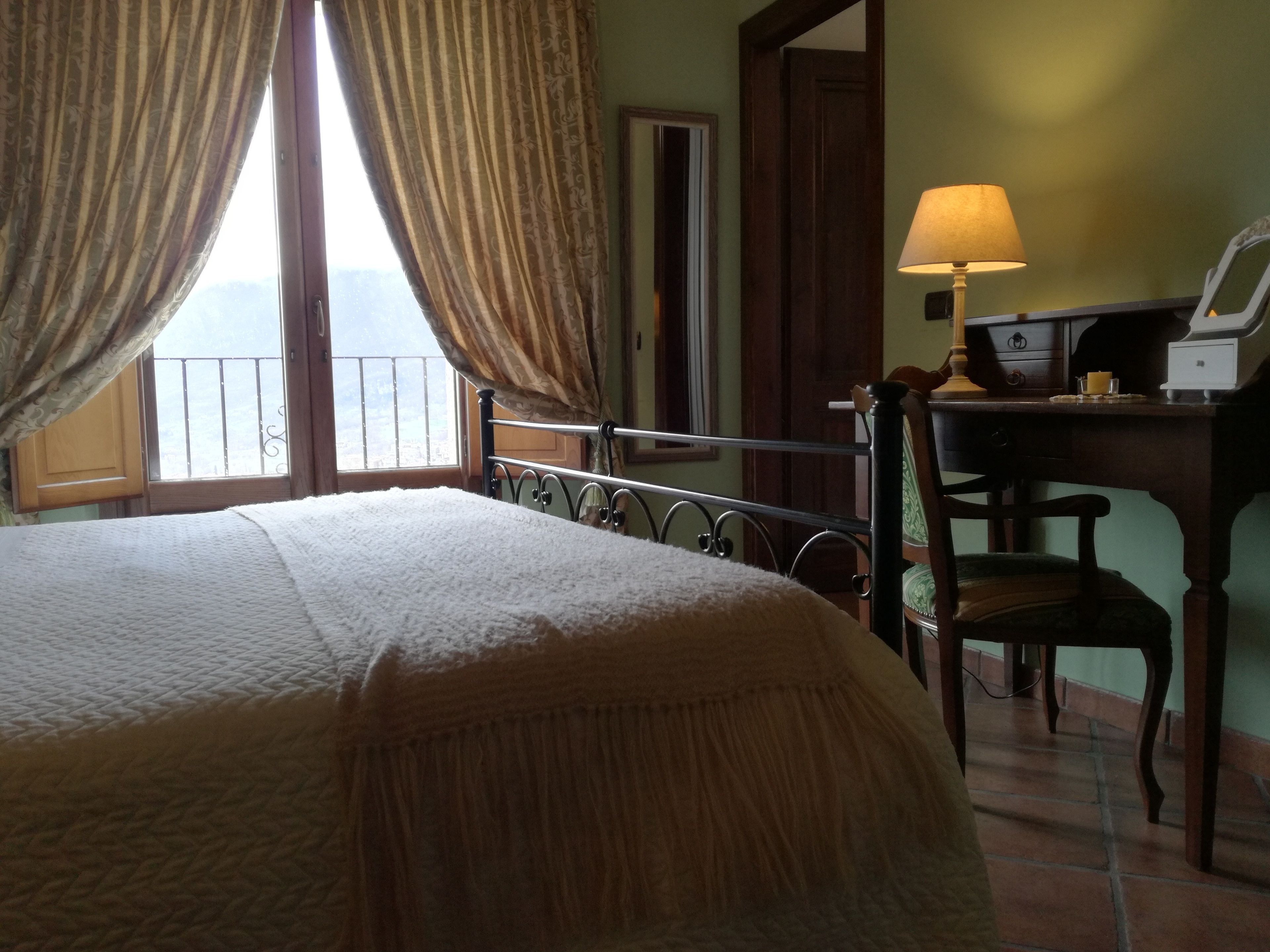 A bedroom with a bed, a desk with a lamp, a chair, and a window with curtains.