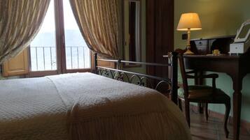 A bedroom with a bed, a desk with a lamp, a chair, and a window with curtains.