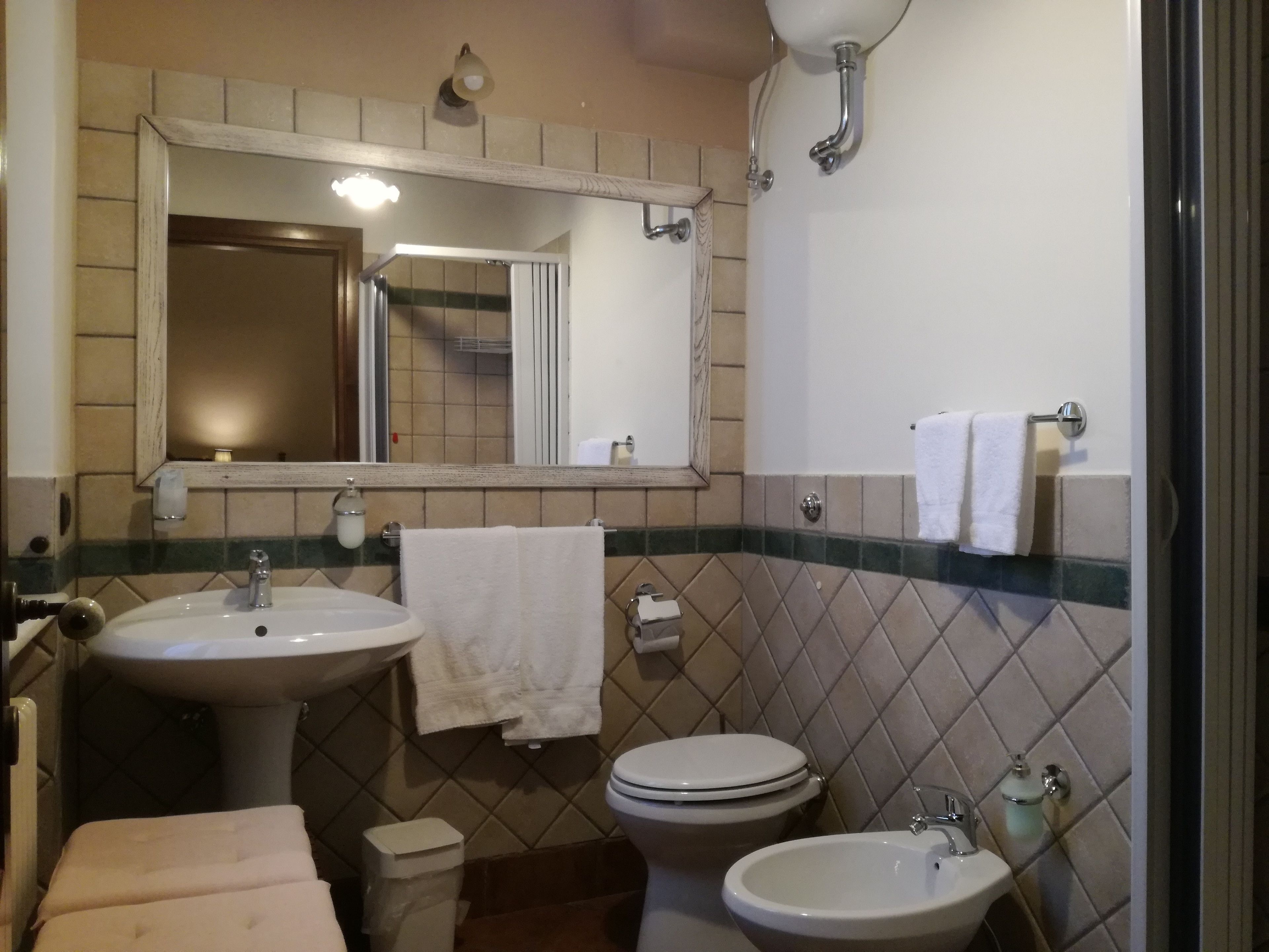 Ein Badezimmer mit Waschbecken, Toilette und Bidet. Über dem Waschbecken hängt ein Spiegel und an der Wand ist ein Handtuchhalter.