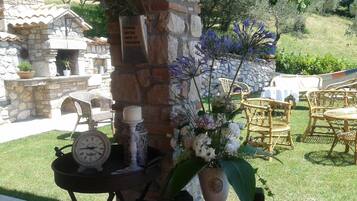 Un muro de piedra con una placa, sillas de mimbre, una mesa con un reloj y un arreglo floral.