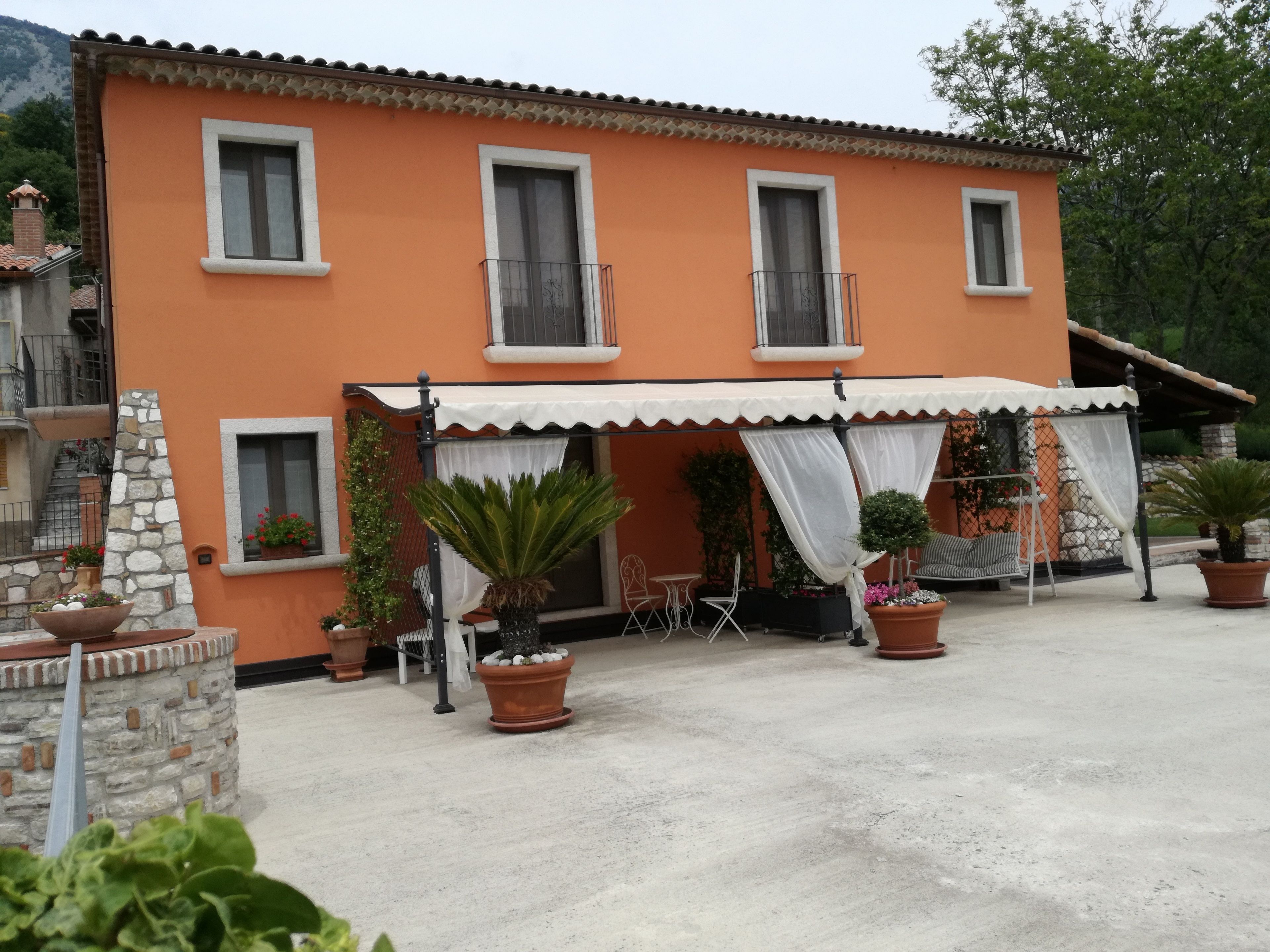 A two-story building with a tiled roof, a balcony, and a covered outdoor seating area with tables and chairs.