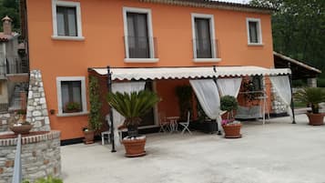 A two-story building with a tiled roof, a balcony, and a covered outdoor seating area with tables and chairs.
