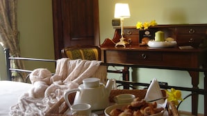 Una cama bien tendida con una cesta de artículos de desayuno, una lámpara y una silla en una habitación con muebles de madera.
