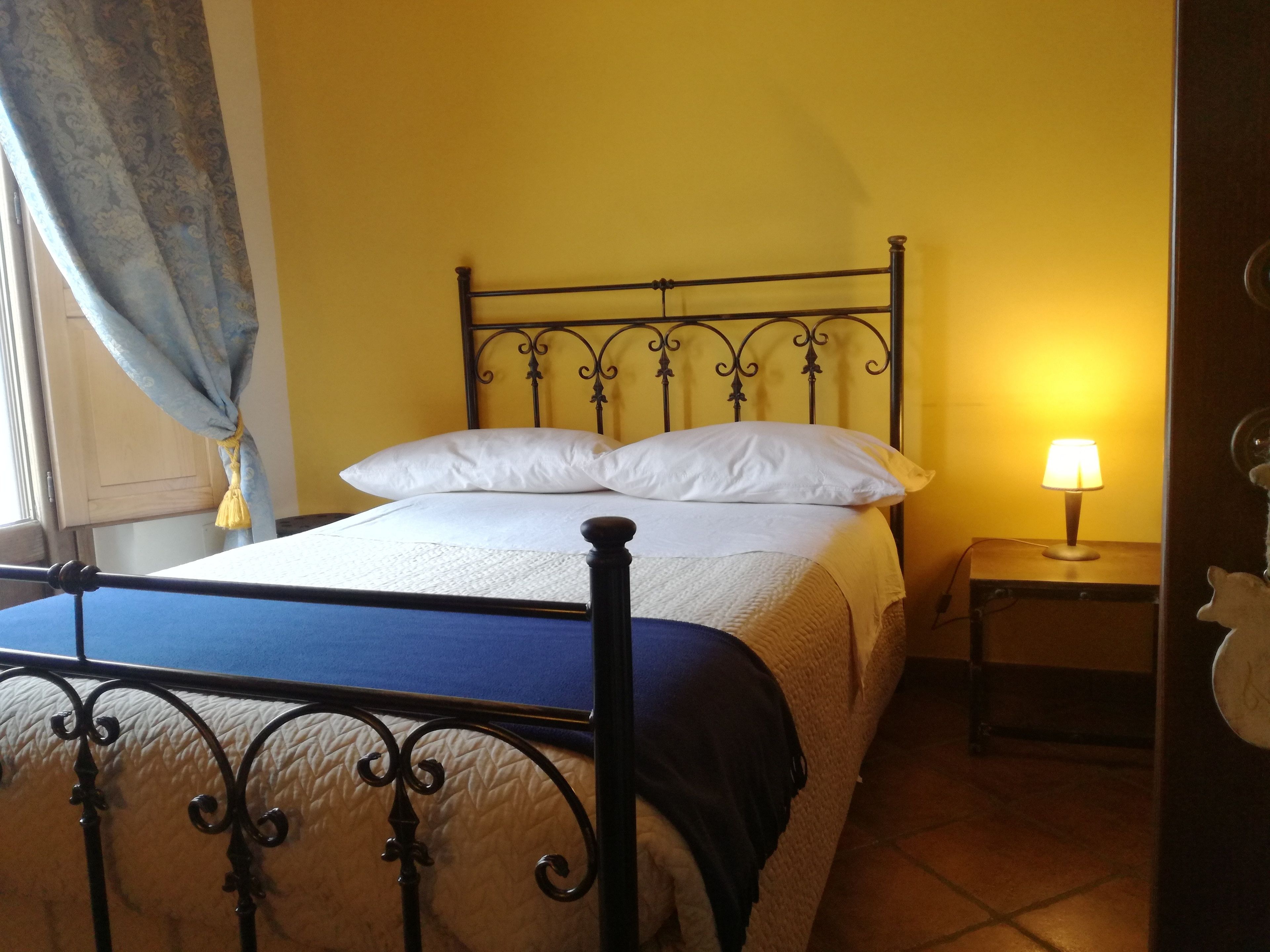 Ein Bett mit Metallgestell, ein Nachttisch mit Lampe und ein Vorhang.