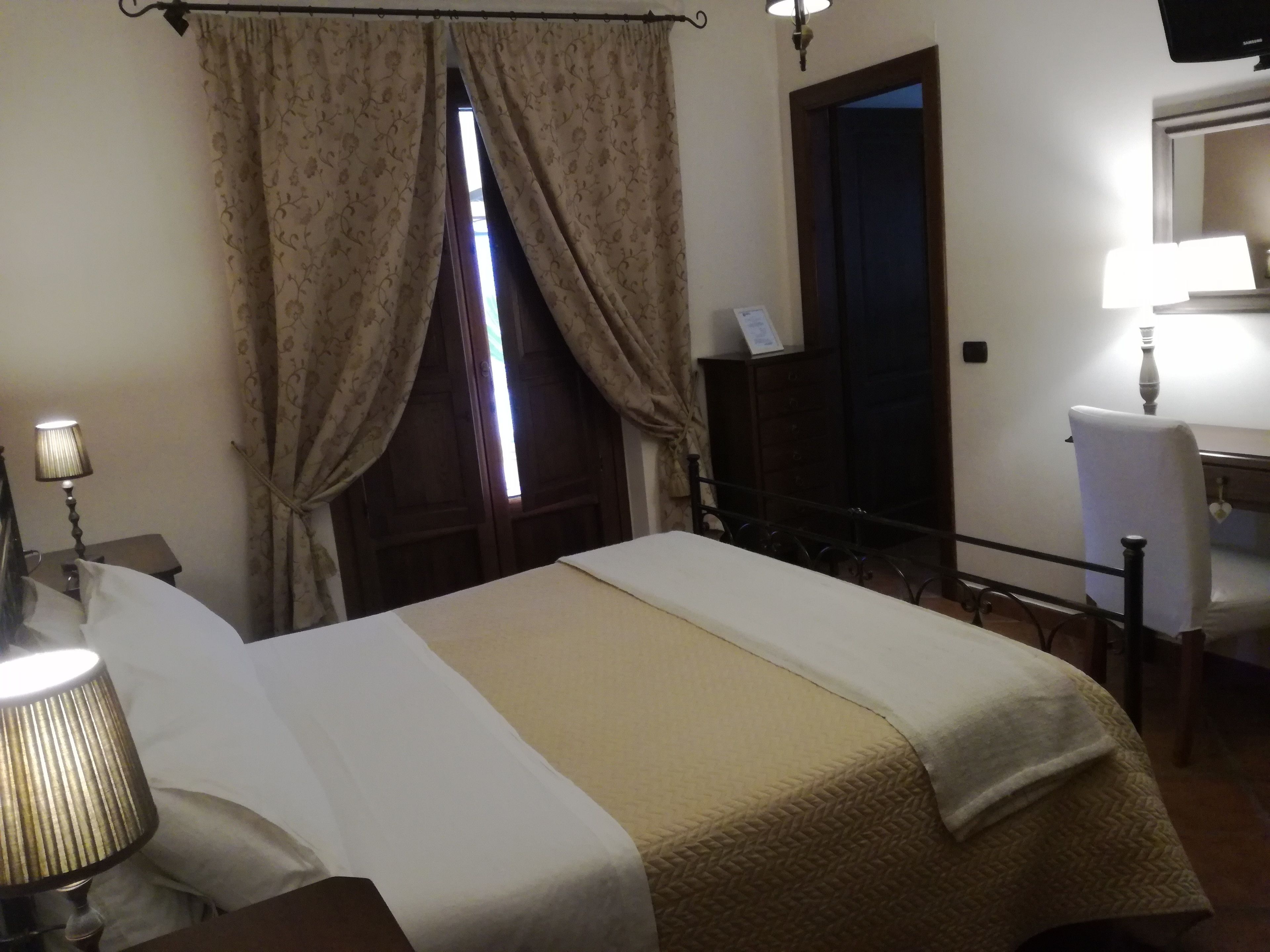 A hotel room with a bed, a desk, a chair, a lamp, and a window with curtains.
