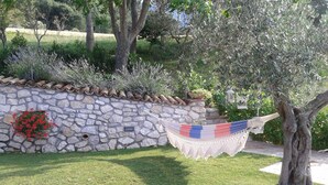 Un muro de piedra con una hamaca, un árbol y un parterre de flores.