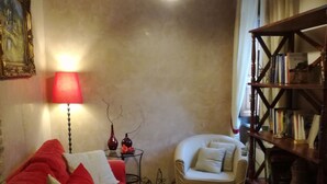Una sala de estar acogedora con un sofá rojo, un sillón blanco, una estantería de madera y una mesa con un cuenco y un posavasos de encaje.