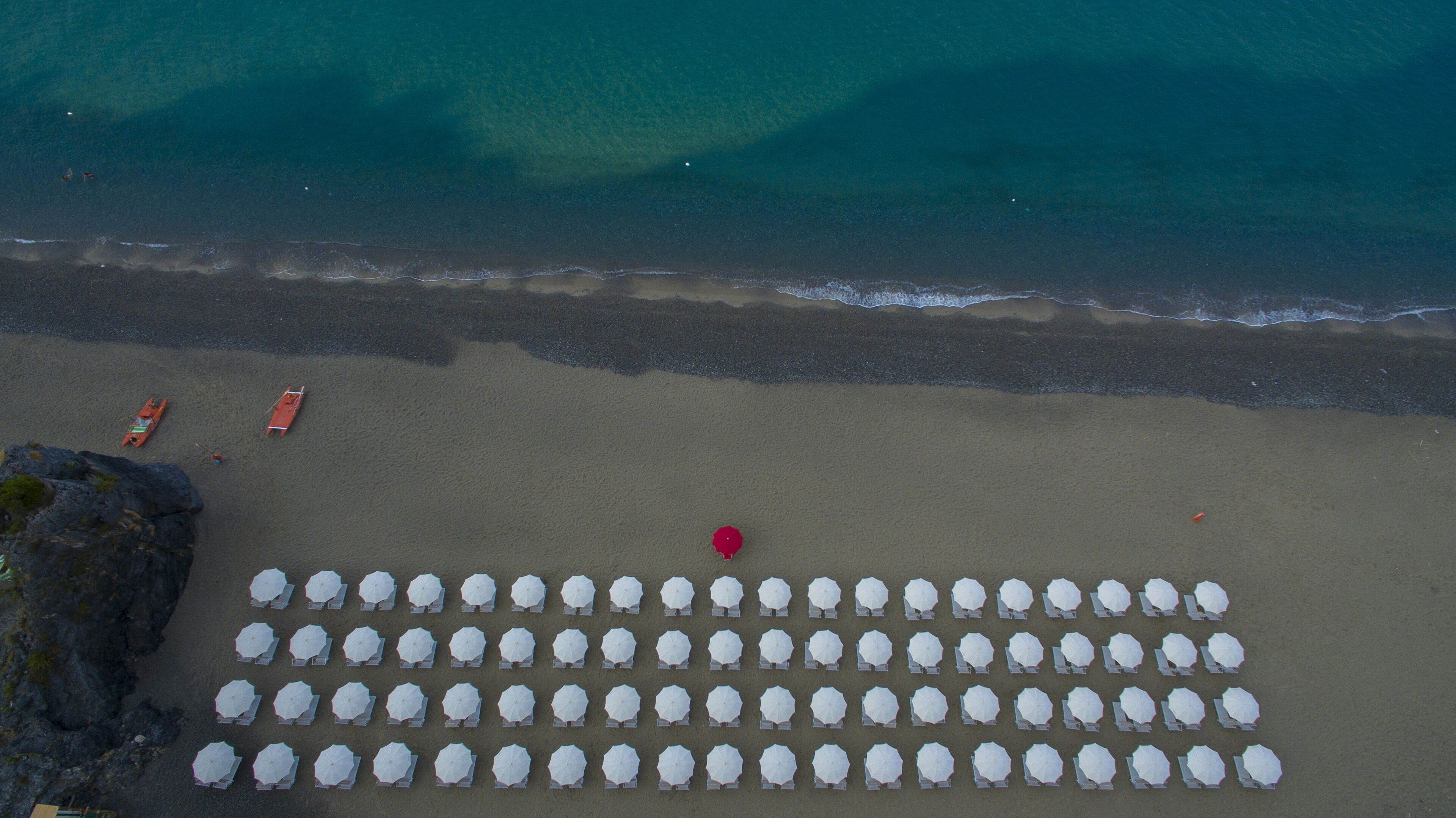 An aerial view of a beach with rows of white umbrellas and a few boats.