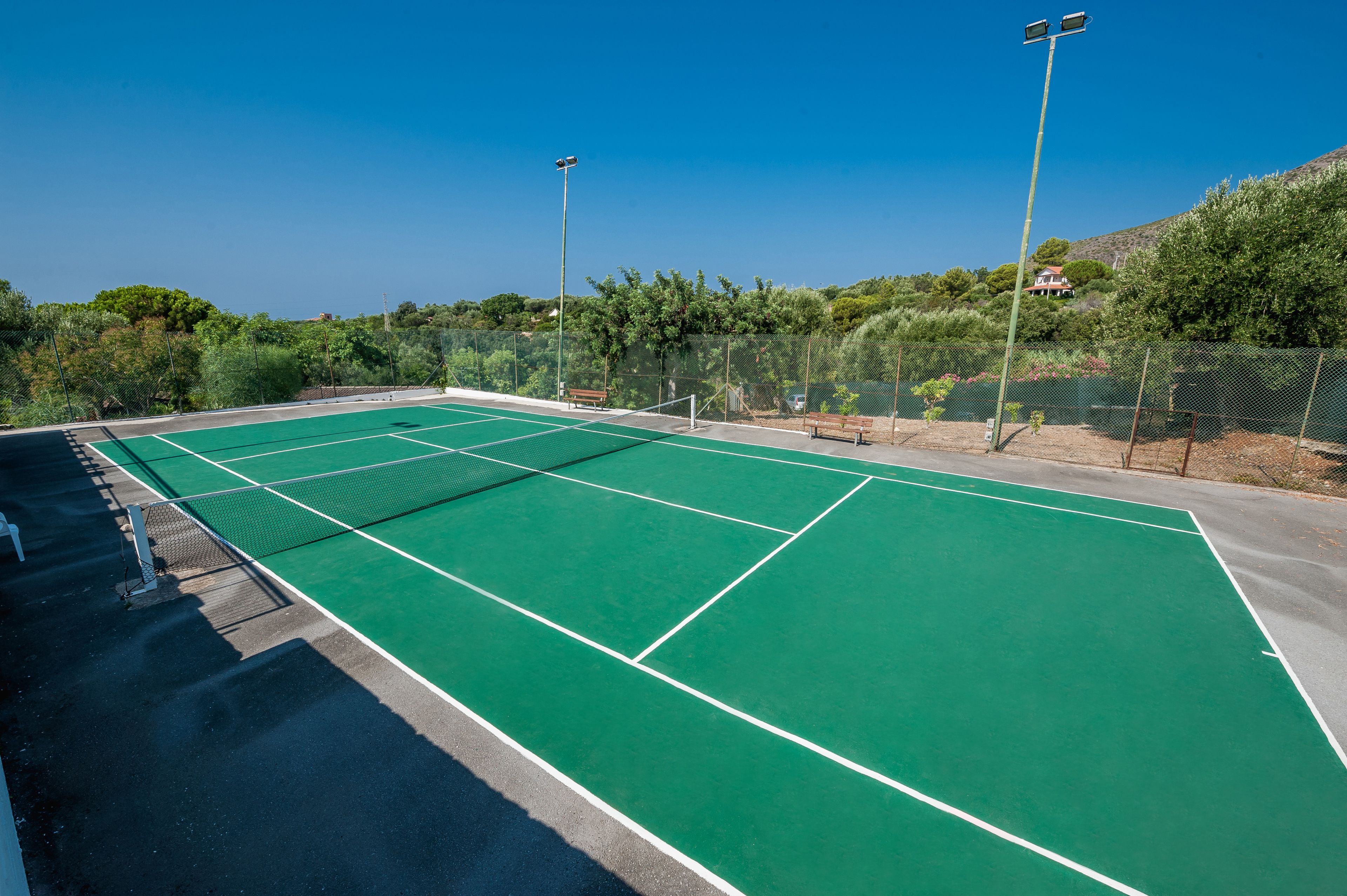 Un court de tennis doté d’une surface verte, entouré d’une clôture, et bordé de bancs.