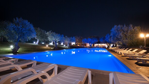 Una piscina con sillas de descanso e iluminación nocturna entre árboles.
