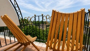 Two wooden chairs on a balcony with a metal railing and a view of greenery.