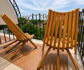 Two wooden chairs on a balcony with a metal railing and a view of greenery.