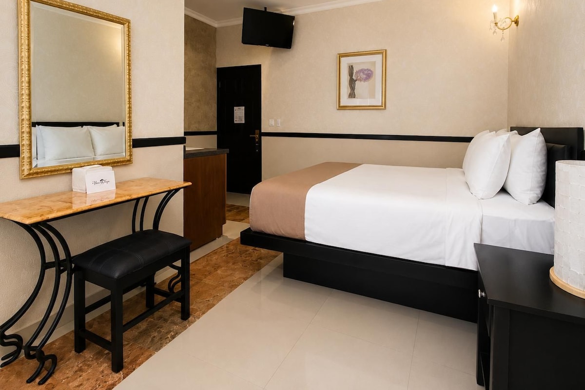 A hotel room with a bed, a desk, a chair, a TV, and a framed picture on the wall.
