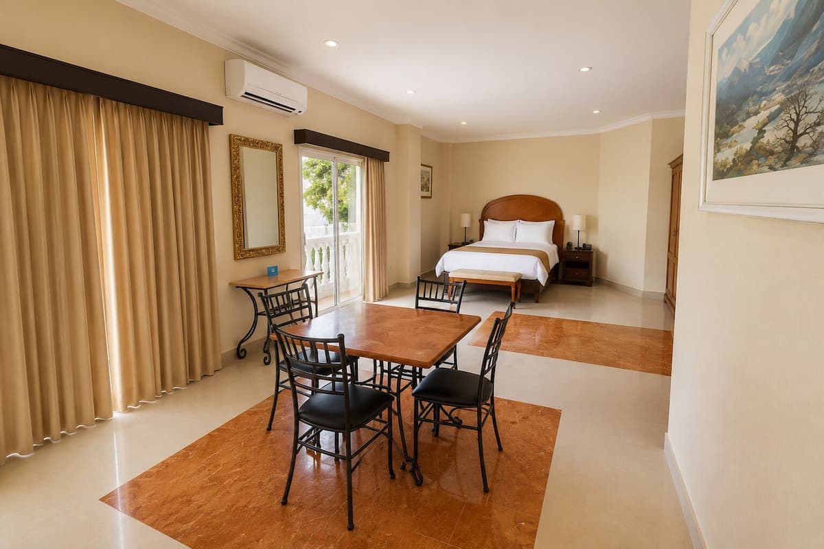 A hotel room with a bed, a dining table with chairs, a small desk, and a window with curtains.
