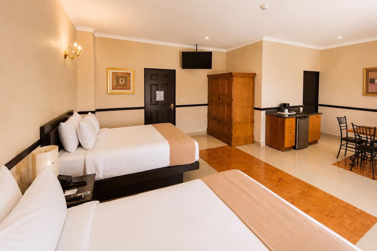 A hotel room with two beds, a desk with a chair, a wardrobe, and a television.
