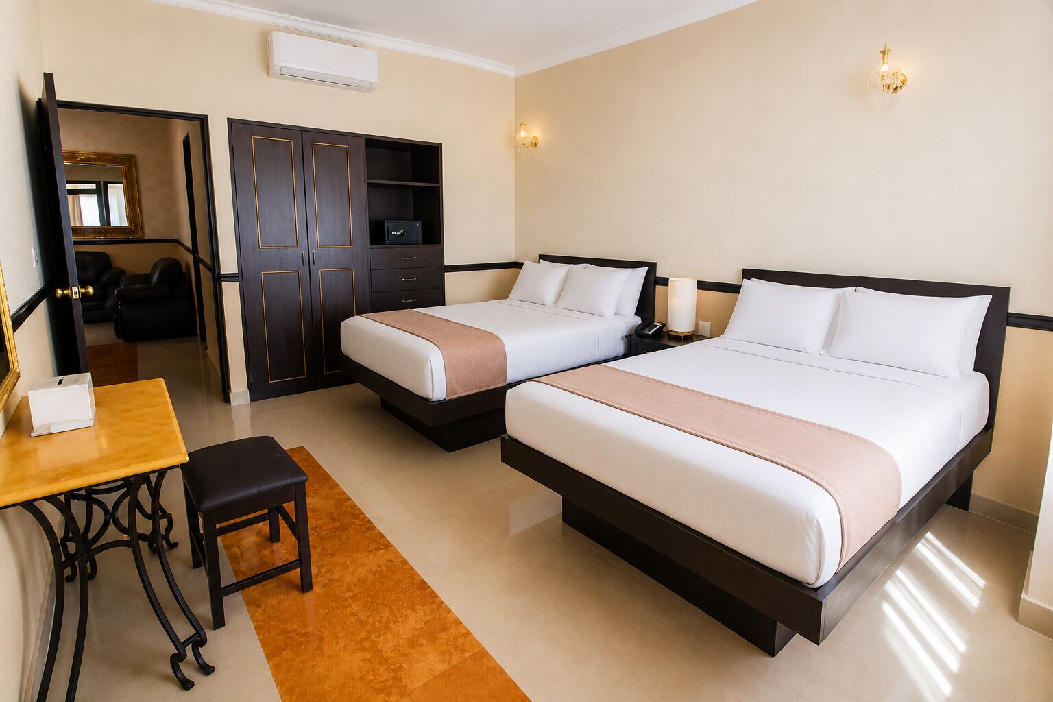 A hotel room with two beds, a desk, a wardrobe, and a mirror.