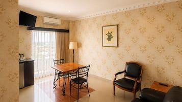 Habitación de hotel con una mesa de comedor, sillas, un sofá, un televisor, un aire acondicionado y un cuadro en la pared.