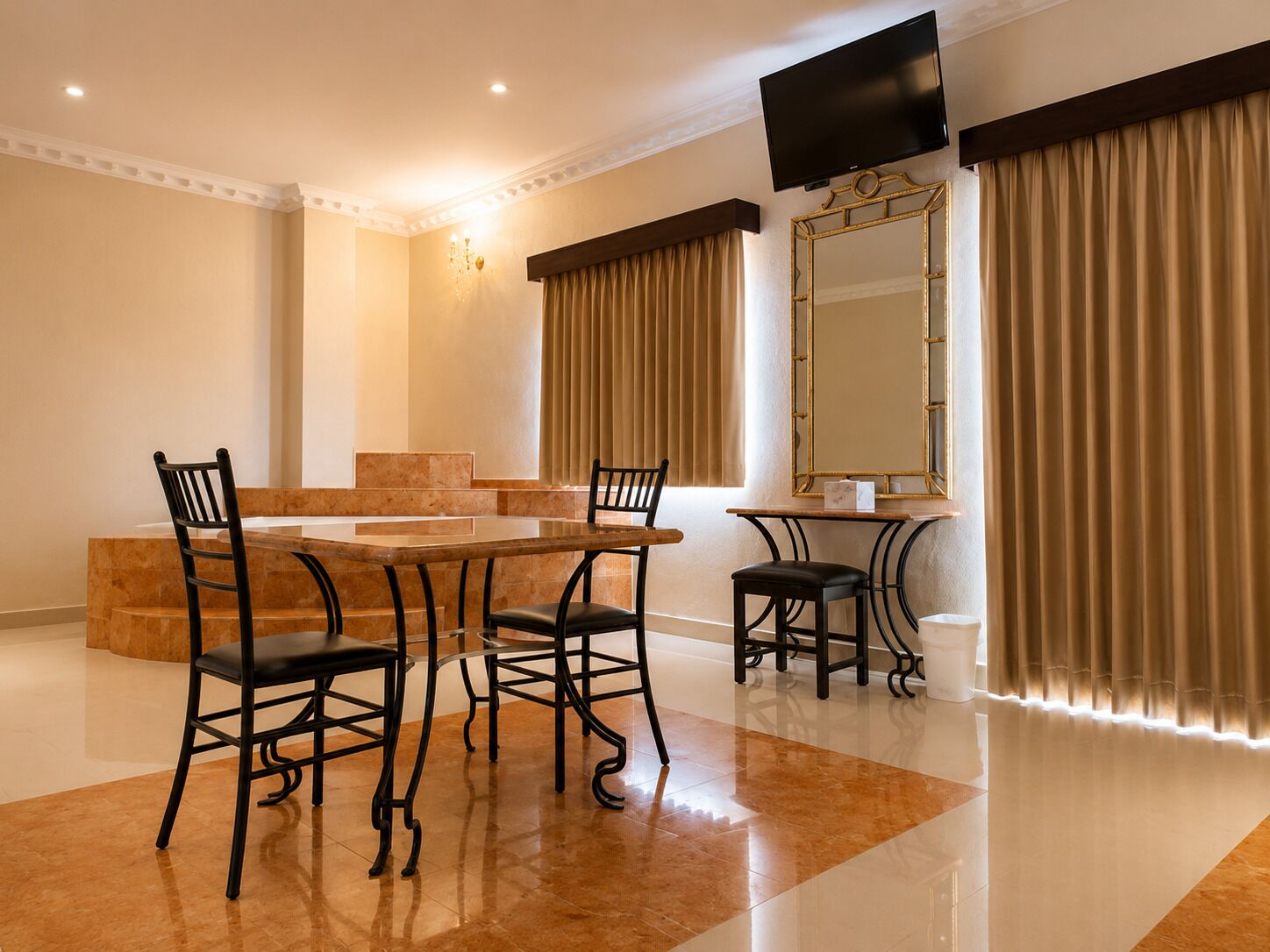 A dining area with a glass table, four chairs, a television, a large mirror, and curtains.