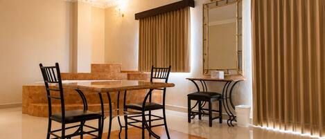 A dining area with a glass table, four chairs, a television, a large mirror, and curtains.