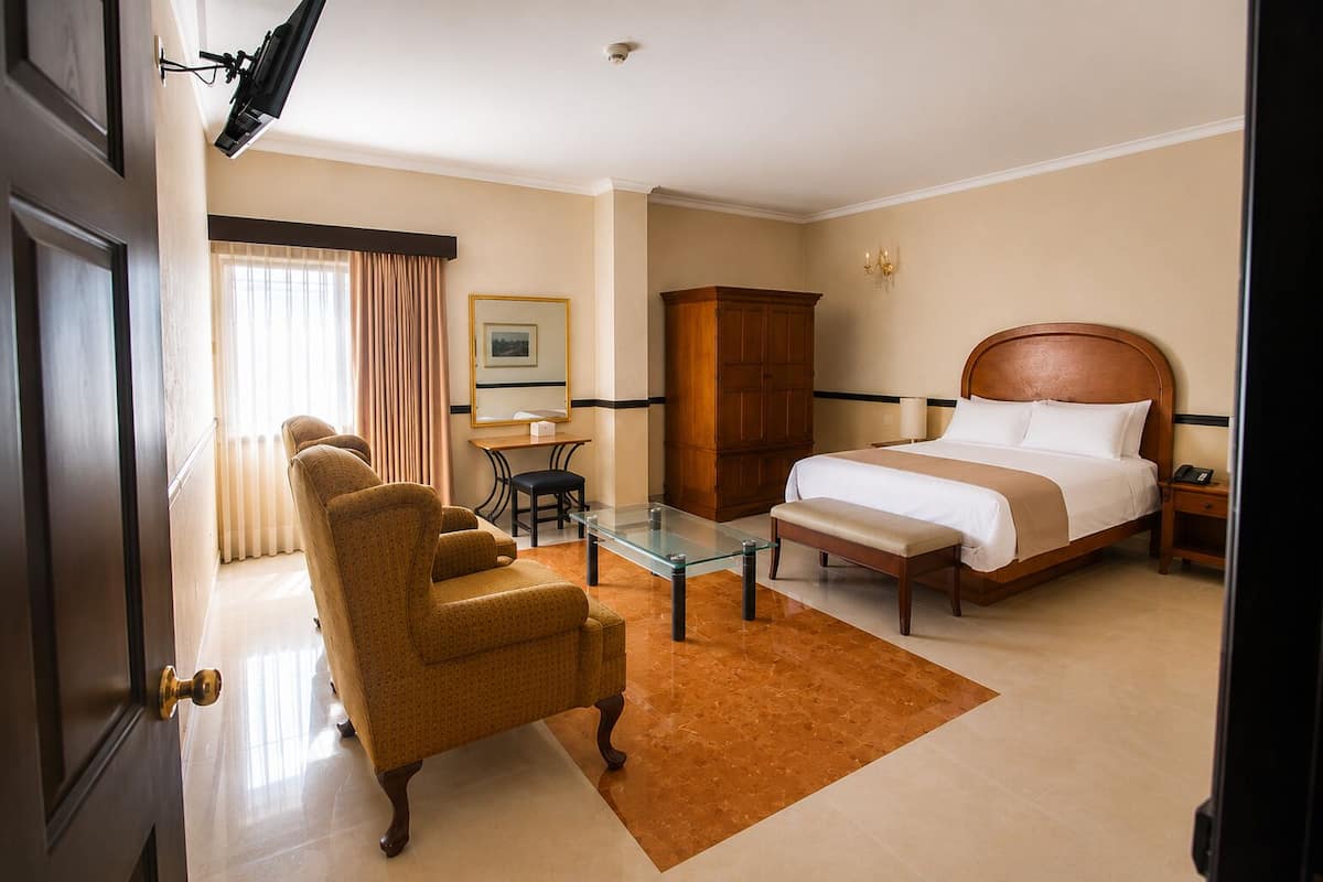 A hotel room with a bed, a chair, a table, a cabinet, and a desk.