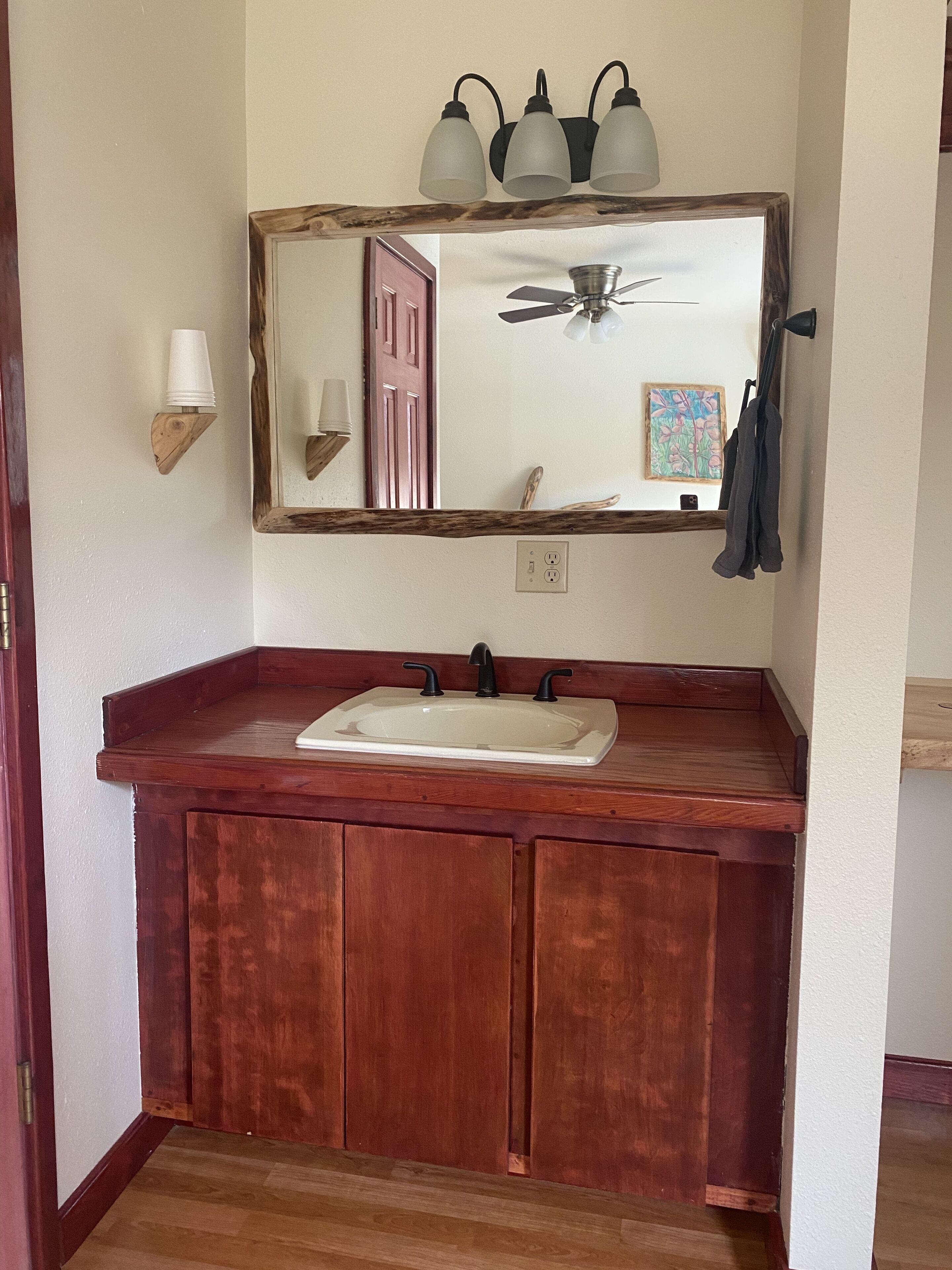 A bathroom with a wooden vanity, a white sink, and a mirror with three lights.