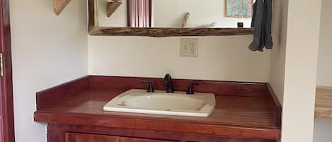 A bathroom with a wooden vanity, a white sink, and a mirror with three lights.