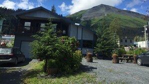A two-story building with a balcony, surrounded by greenery and a mountain in the background.