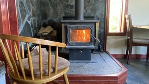 A stone wall, a wooden chair, a fireplace with a visible fire, and a window with daylight.