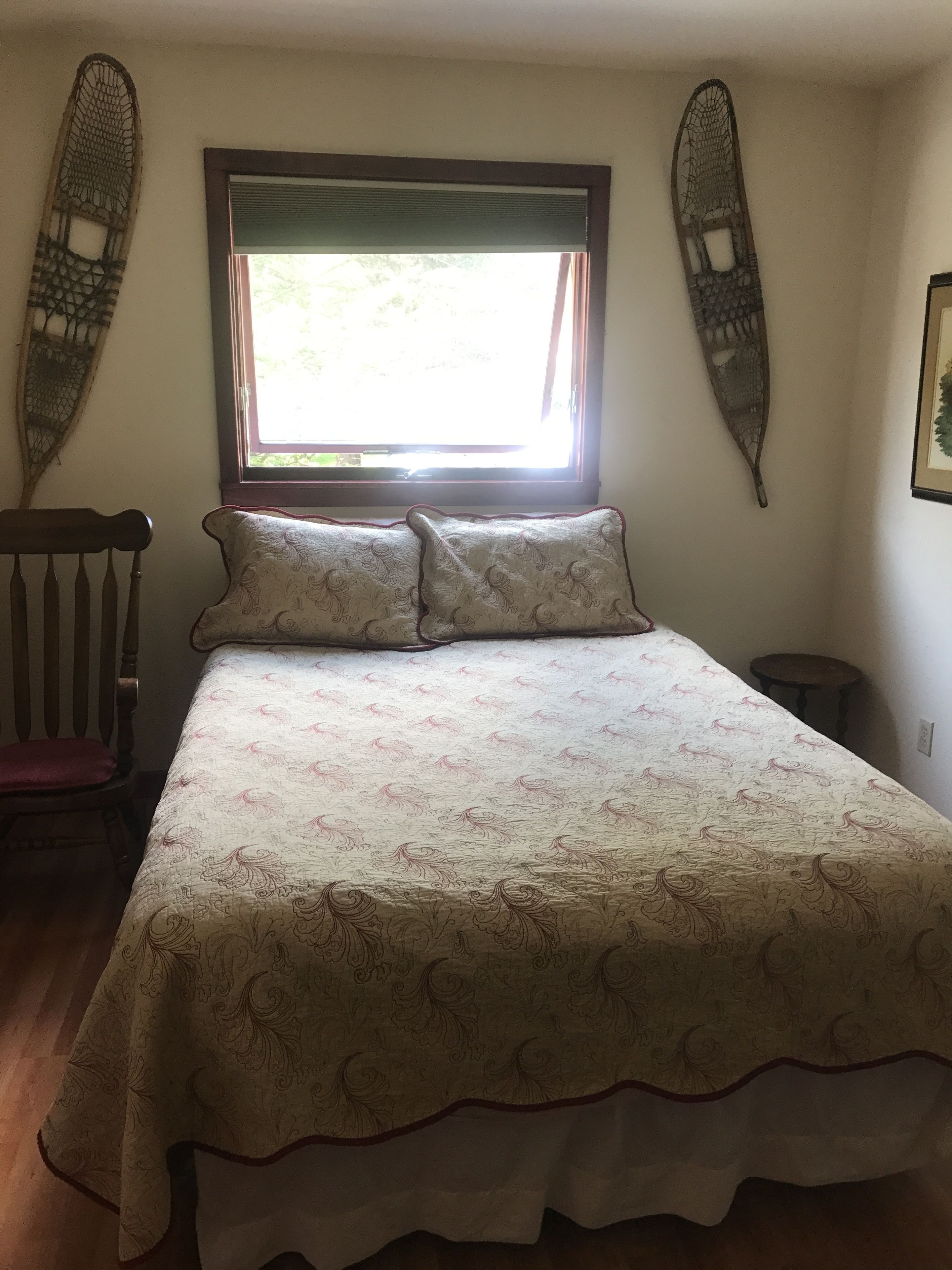 Quarto com cama, uma cadeira, janela e decorações nas paredes.