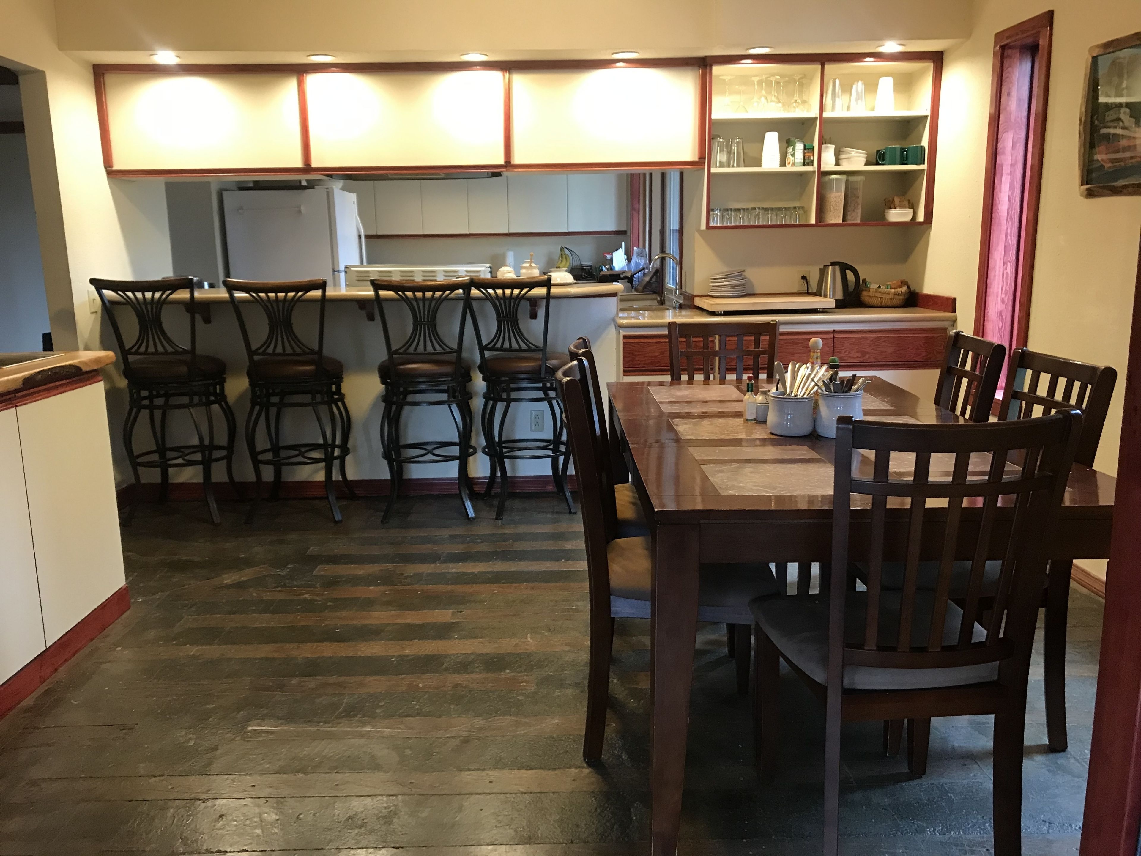 A kitchen with a dining table, four bar stools, and a refrigerator.