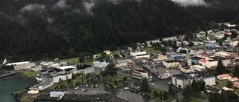 A coastal town with a marina, buildings, and a forested mountain backdrop.