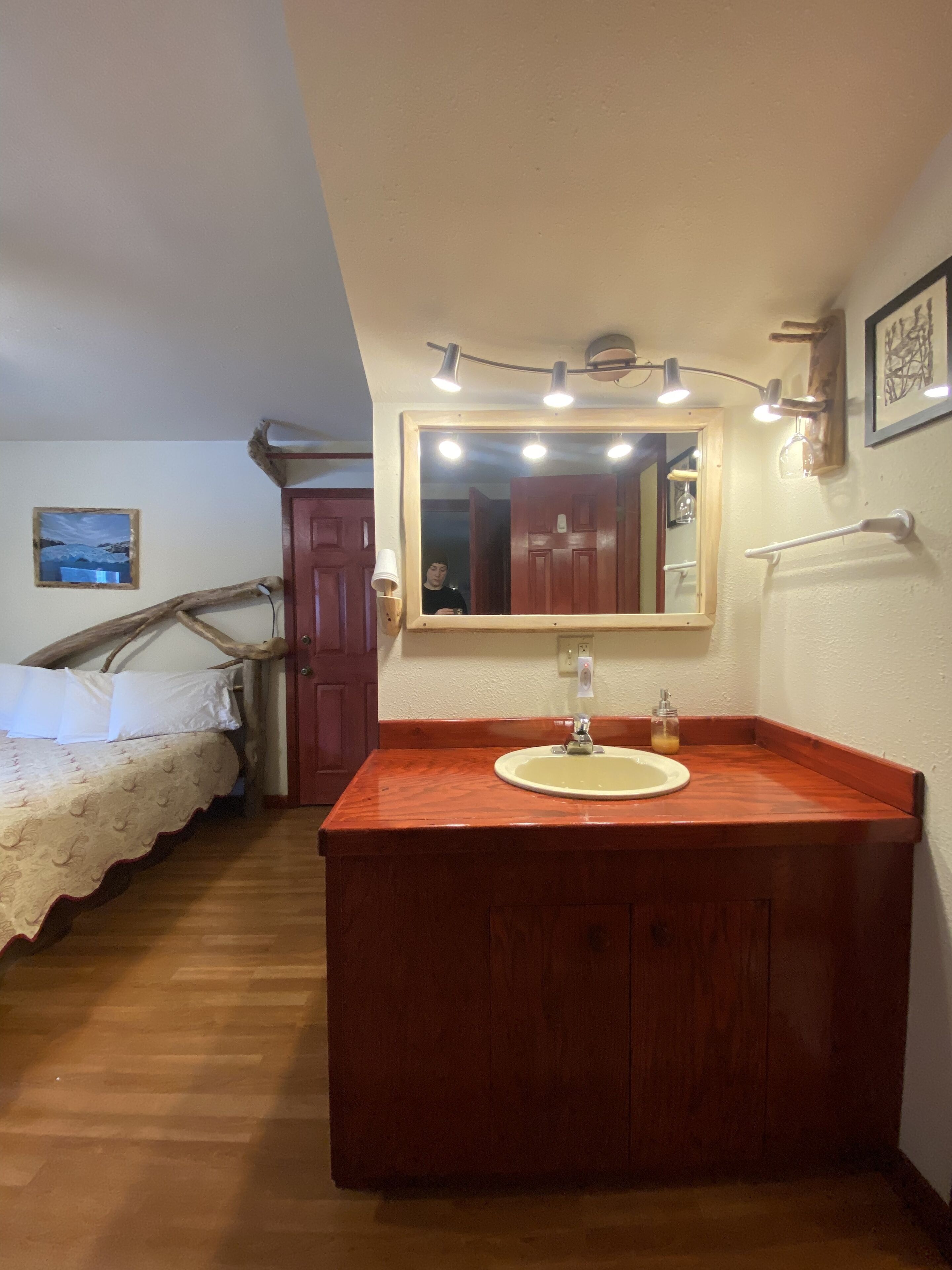 Une chambre à coucher avec un lit en bois, une coiffeuse en bois dotée d’un lavabo, un miroir et une porte en bois.