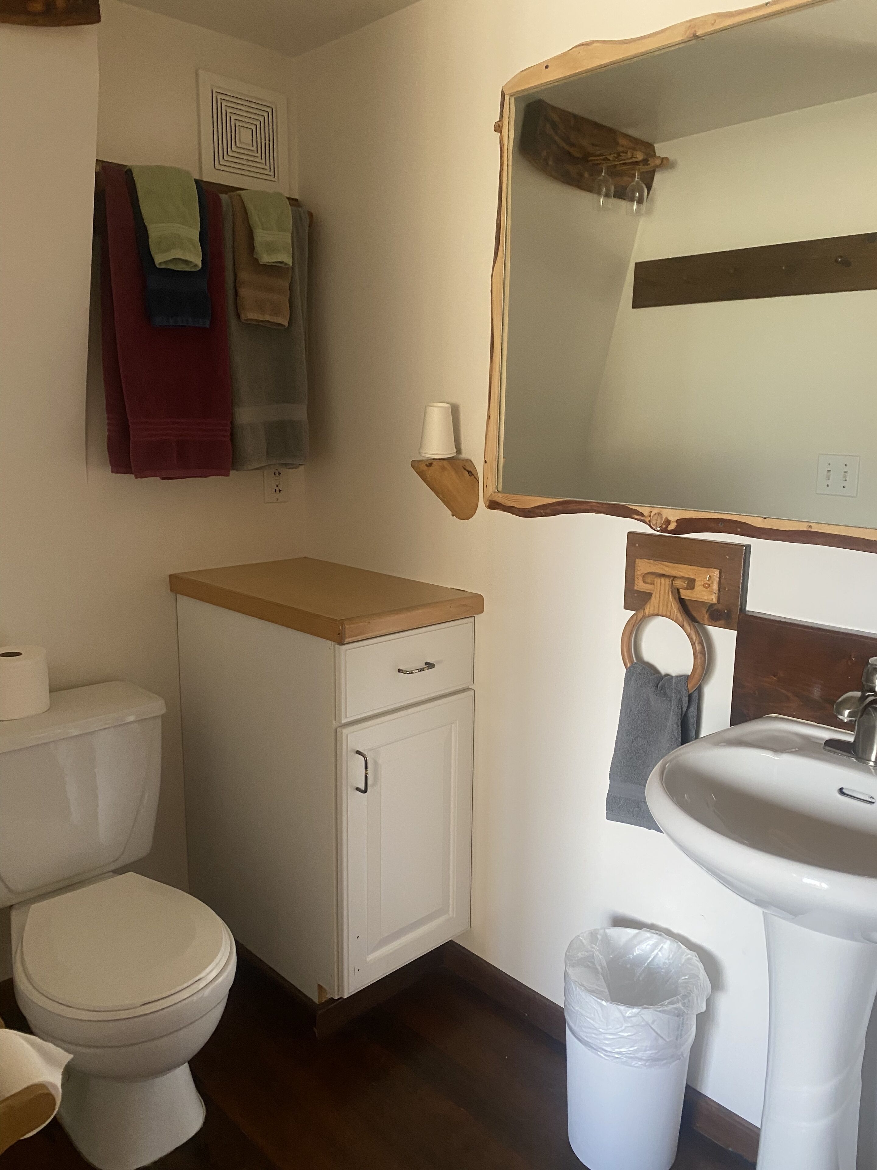 Een badkamer met toilet, wastafel en spiegel. Handdoeken hangen aan een rek en er staat een prullenbak.