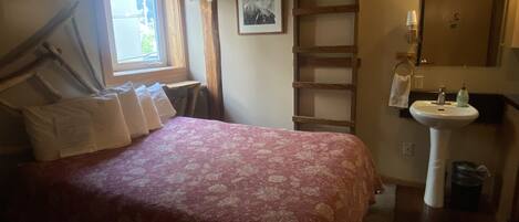 A bedroom with a bed, a window, a ladder, a sink, and a mirror.