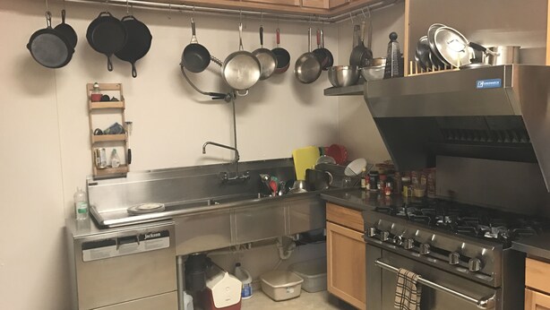 Een keuken met roestvrijstalen apparatuur, houten keukenkastjes en diverse pannen die aan de muur hangen.