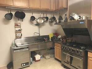 A kitchen with stainless steel appliances, wooden cabinets, and various pots and pans hanging on the wall. - A Swan Nest Inn (Seward)