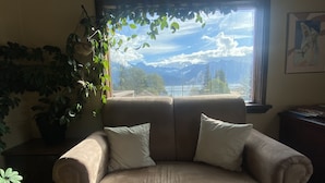 Een beige fauteuil met twee kussens, voor een raam met uitzicht op bergen en bomen.