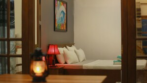 A hotel room with a bed, a nightstand with a red lamp, a wall-mounted air conditioner, and a colorful abstract painting. - Temple Tree Hotel Weligama (Weligama)