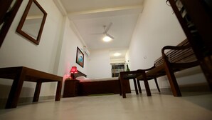 A room with a bed, a desk, a chair, a standing fan, and a mirror on the wall. - Temple Tree Hotel Weligama (Weligama)