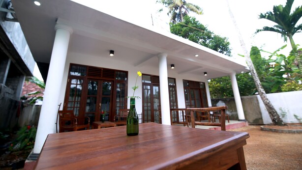 An outdoor wooden table with a green bottle and a yellow flower. - Temple Tree Hotel Weligama (Weligama)