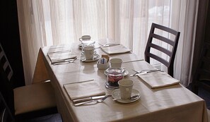 A neatly set dining table with a long rectangular tablecloth, multiple cups, saucers, and a glass container. - Ansharius (Roccaraso)