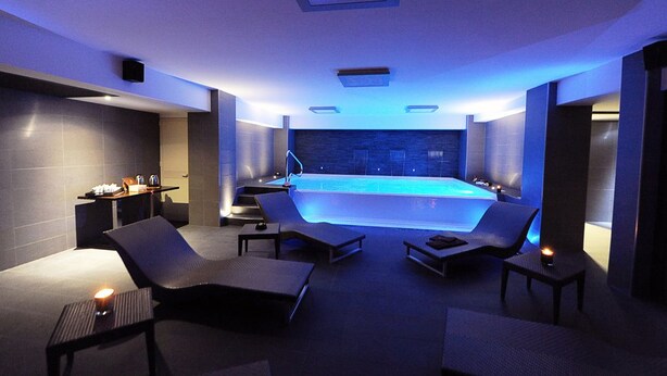 Une salle de spa moderne dotée d’une grande piscine chauffée, de chaises longues et d’une petite table avec des accessoires.