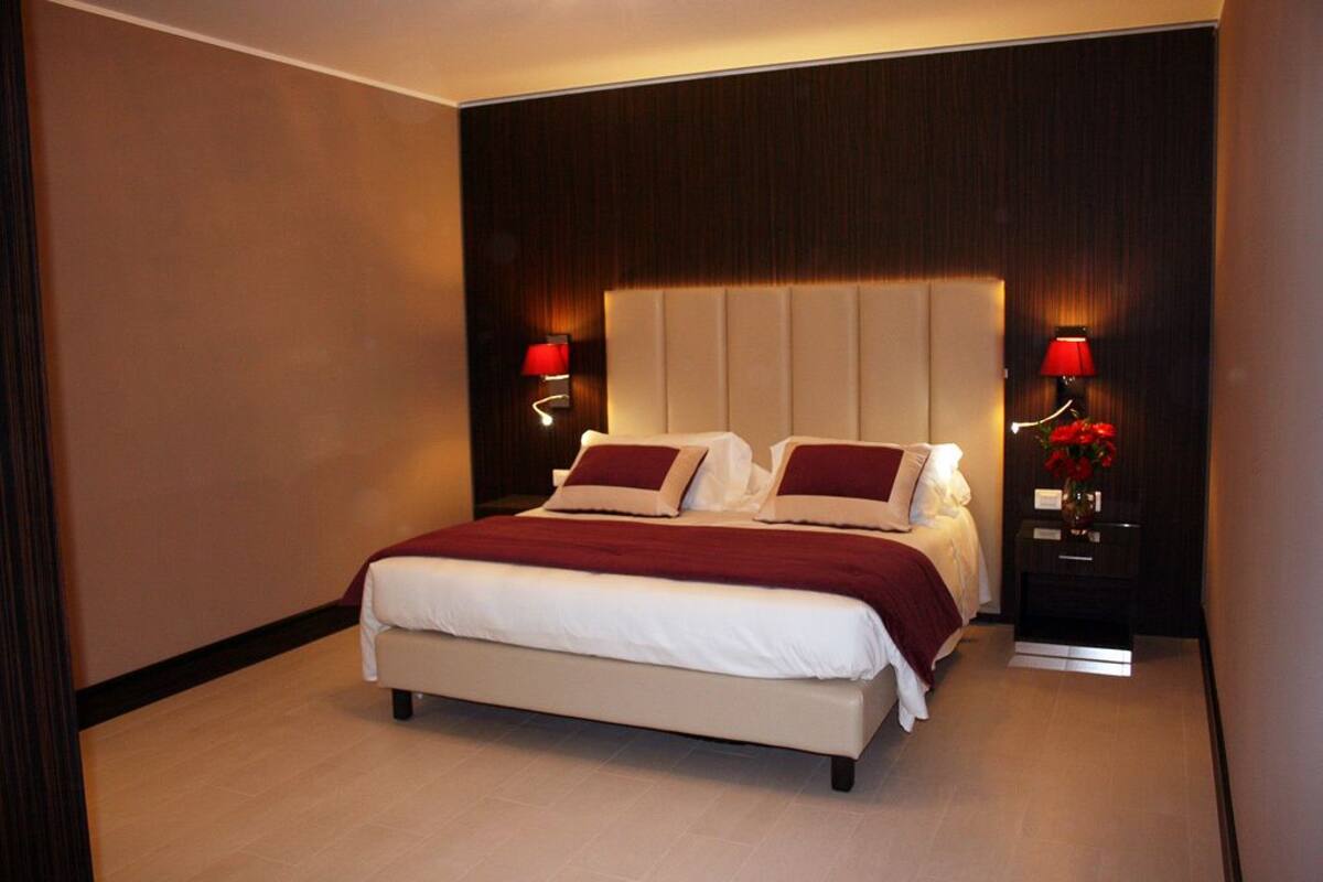 Una habitación de hotel moderna con una cama grande, dos mesitas de noche con lámparas y un cabecero de madera oscura.