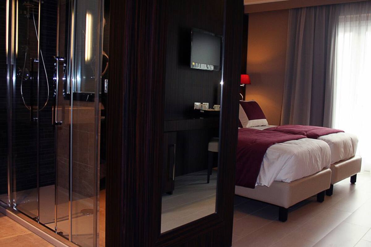 Habitación de hotel con cama, escritorio, televisión y zona de ducha.