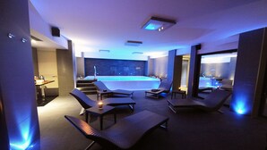 Un espace piscine intérieur moderne, doté de chaises longues et d’une petite table, d’un escalier menant à un niveau supérieur et d’un espace lavabo bien visible.